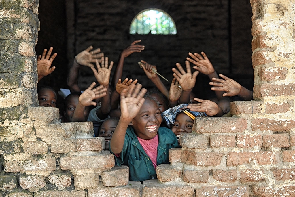 A group of african children inside of a destroyed school, wave hands and say hello.